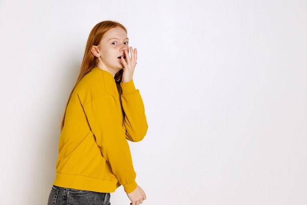 Portrait of emotive teen girl in yellow sweater posing isolated over white studio background