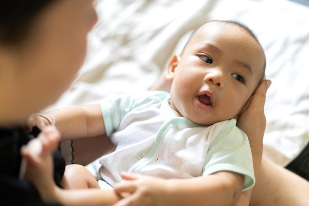 Portrait of enjoy happy love family asian mother playing with adorable little asian babyMom touching with cute son moments good time in a white bedroomLove of family concept