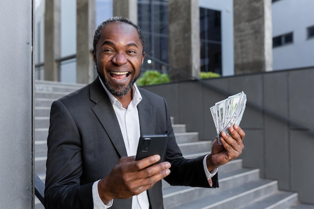 Portrait of an enthusiastic senior businessman in a suit standing outside an office bank he is