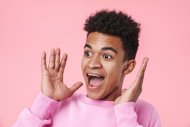 Portrait of an excited african teenager boy wearing pullower standing isolated on pink, screaming