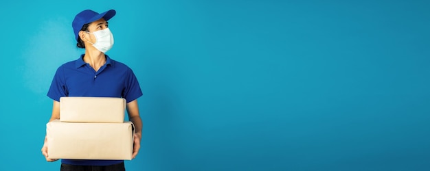 Portrait of excited delivery man in blue uniform holding parcel box isolated over blue background