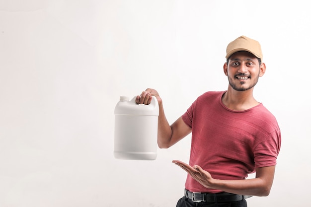 Portrait of a excited happy young delivery man in cap standing over white background and holding bottle in hand.