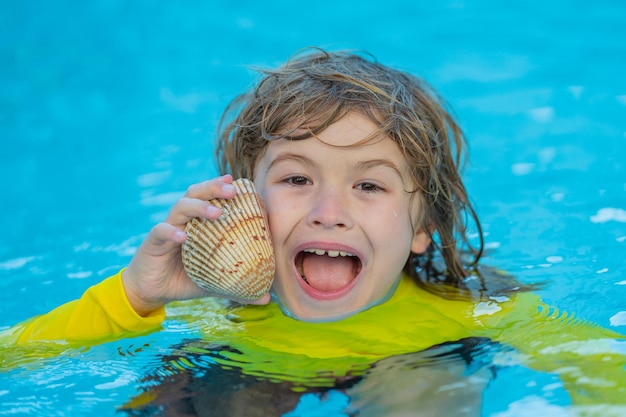 Portrait of excited kid holding seashells swim in sea water Cute child playing with shell outdoor on summer beach Little boy holding a sea shell Summer vacation concept