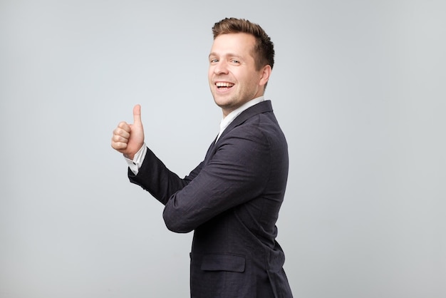 Portrait of excited man in suit giving thumb up against gray background