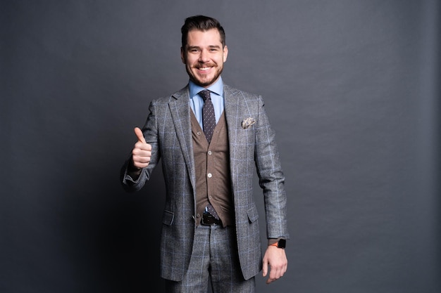 Portrait of excited satisfied cheerful confident positive handsome demonstrating thumbs-up pointing up isolated on gray background.