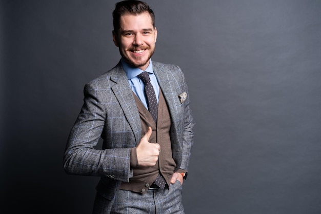 Portrait of excited satisfied cheerful confident positive handsome demonstrating thumbs-up pointing up isolated on gray background.