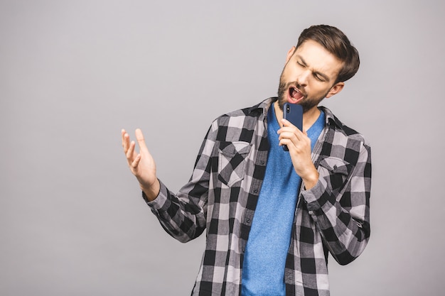 Portrait of an excited young man in t-shirt isolated over gray wall, holding blank screen mobile phone, singing.