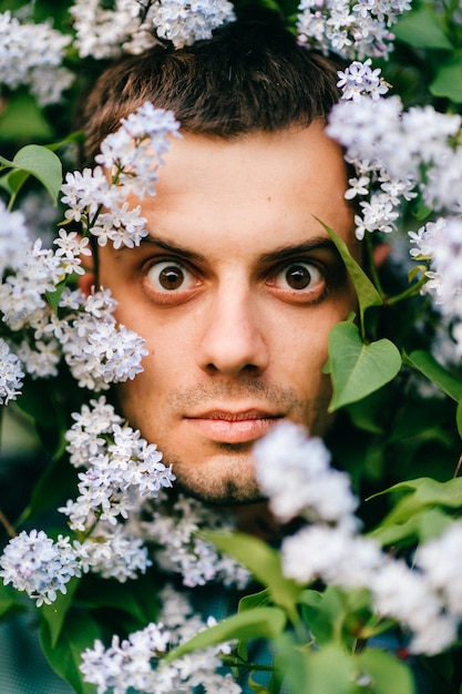 Portrait of expressive male through blooming lilac bushes