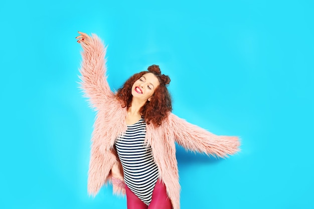 Portrait of expressive young model in pink fur coat on blue background