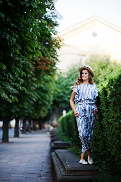 Portrait of a fabulous young woman in striped overall walking on the barrier in the park.