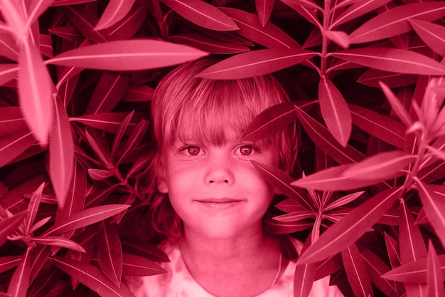 Portrait face of candid happy little kid boy with problem allergic skin on background of red purple pink plants in summer vacation travel allergy toned in viva magenta trend color of the year 2023