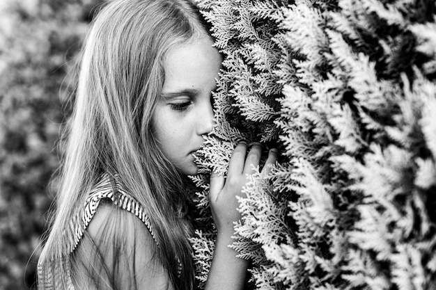 Portrait face of candid offended upset little kid girl of eight years old with long blond hair on background of plants during summer vacation travel gen z mental health concept toned in white black