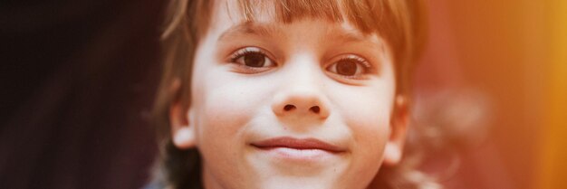 Portrait of the face of cute happy smiling candid little six year old kid boy blond hair looking up at the camera at home lifestyle banner flare