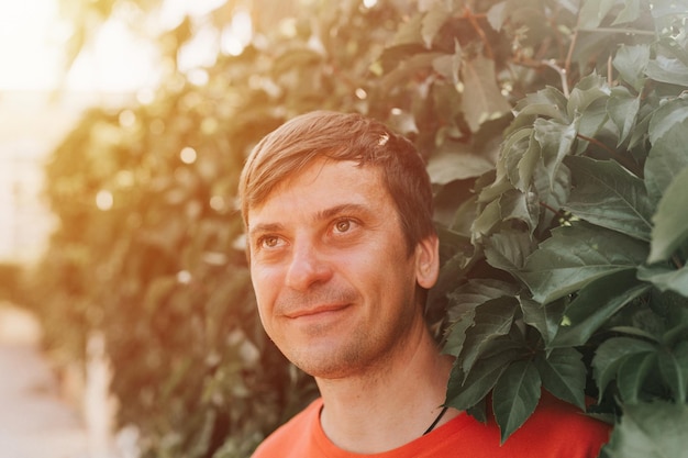 Portrait of face happy smiling mature 40 years man solo traveler with stubble and brown eyes on the background of green trees plants in nature on sunny summer day on vacation travel getaway flare