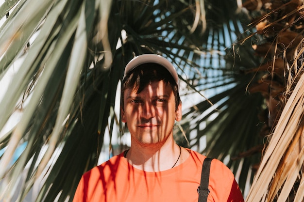 Portrait face happy smiling unshaven mature 40 years man solo traveler with stubble on background of green plant palm leaves in nature on sunny summer day on vacation travel getaway light and shadow