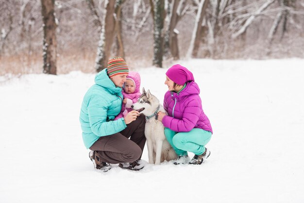 Portrait of family and their pet - husky dog, sitting on the snow in winter day