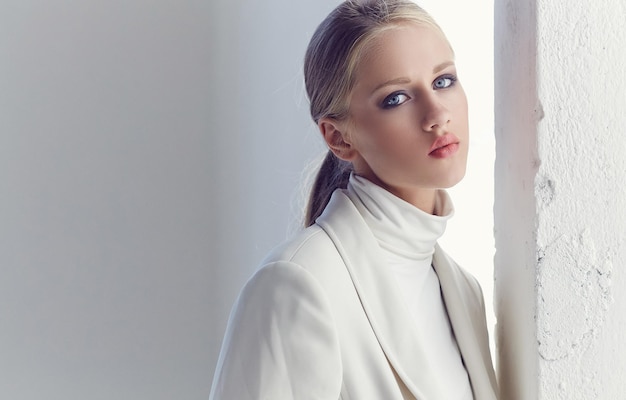 Portrait of fashionable blond girl with blue eyes dressed in white clothes.