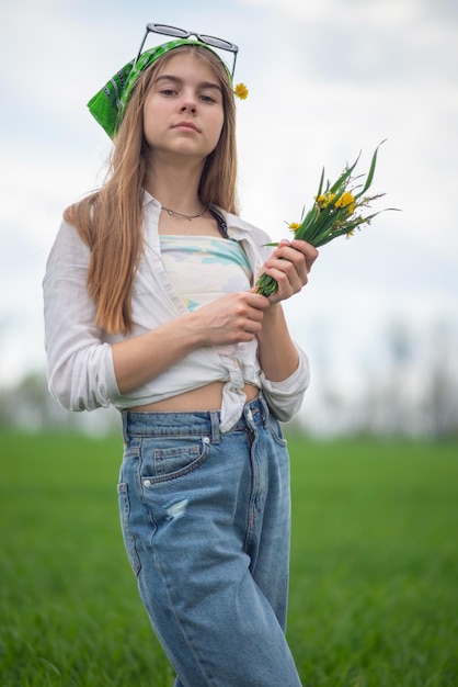 Portrait of a fashionable little girl with a bouquet of wildflowers in a green field against a background of a cloudy sky