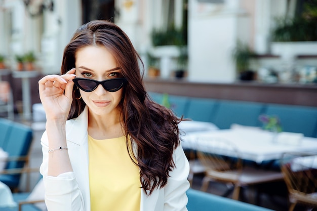 Portrait of fashionable stylish brunette woman in sunglasses in european city fashion summer