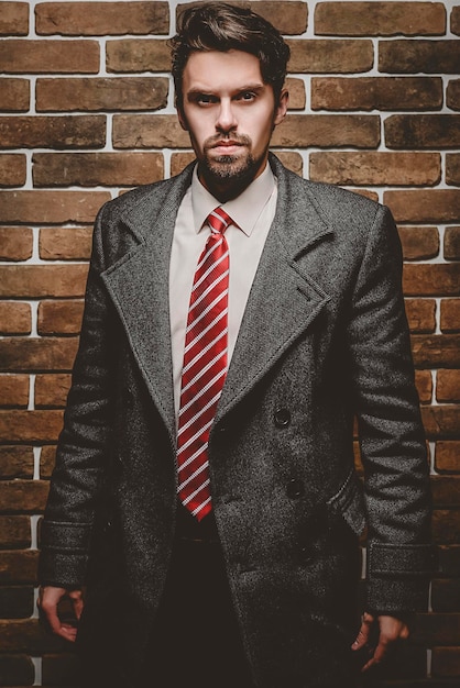 Photo portrait of fashionable well dressed man with beard posing outdoors looking away confident and focused mature man in coat standing on a brick wall background elegant fashion model