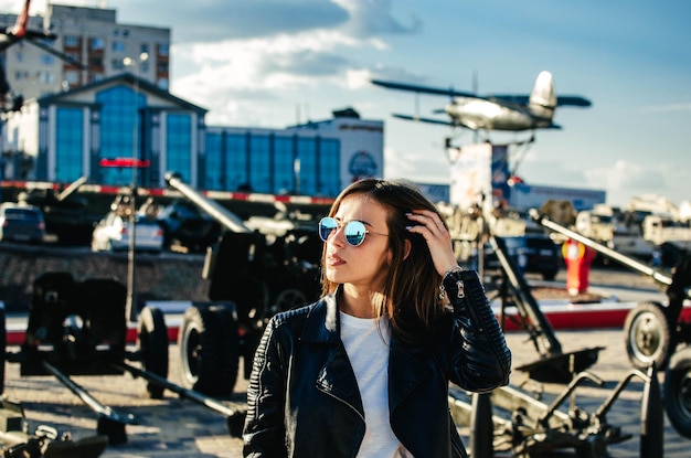 Portrait of a fashionable young woman with sunglasses at the airfield on the background of airplanes