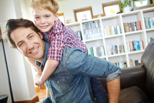 Portrait father and child on sofa with piggyback bonding and love in living room for playful family in home Relax dad and son on couch for happy weekend together with fun smile and embrace