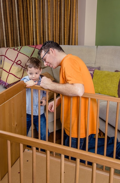 Portrait of father and son assembling together cot for a newborn at home. Family leisure concept