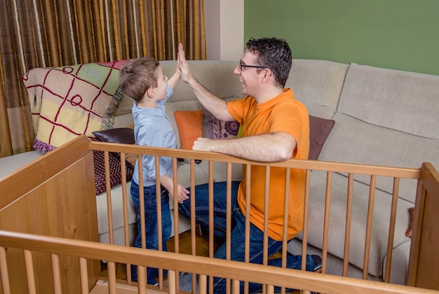 Portrait of father and son giving five for a success in the assembly of cot for a newborn at home. Family leisure concept