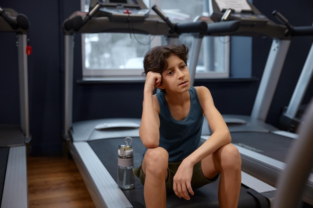 Portrait of fatigue preteen boy having rest after training on treadmill