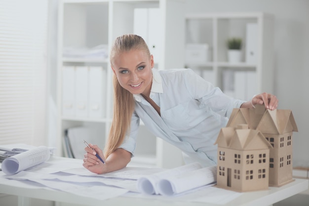 Portrait of female architect with blueprints at desk in office