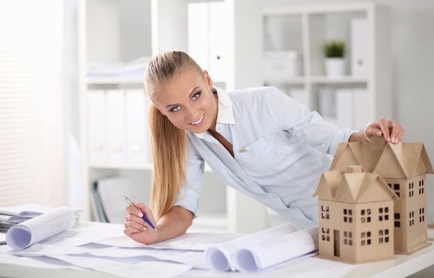 Portrait of female architect with blueprints at desk in office