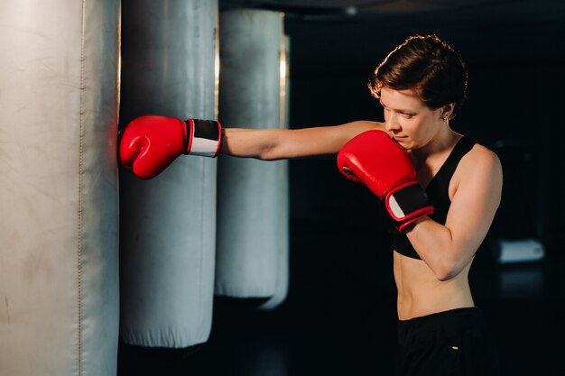 Portrait of a female boxer in red gloves in the gym during training.