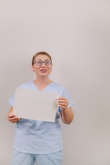 Portrait of a female doctor in a blue robe holding a white blank sheet