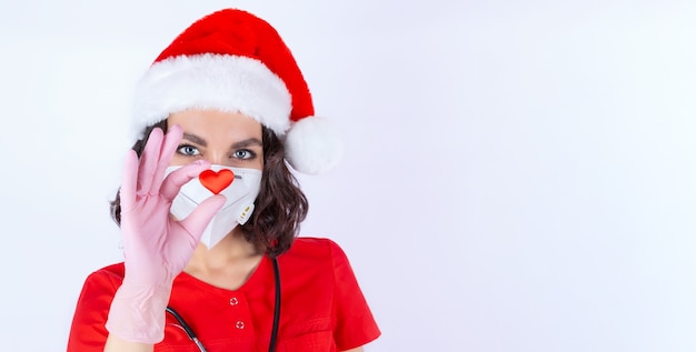 Portrait of a female doctor in a medical mask Santa Claus hat gloves with the image of a heart a symbol of love a healthy heart