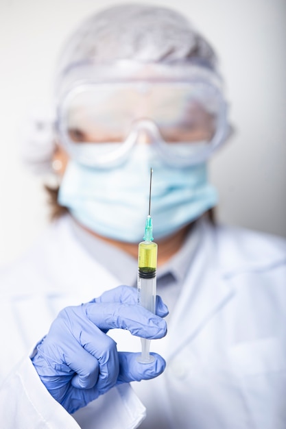 Portrait of female doctor wearing glasses, gloves and protective mask with a syringe in hand for the new vaccine. Selective focus