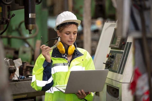 Portrait of female Engineer operating machine by laptop in factory