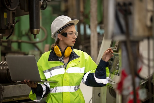 Portrait of female Engineer standing while using laptop computer to operating a machine in factory.