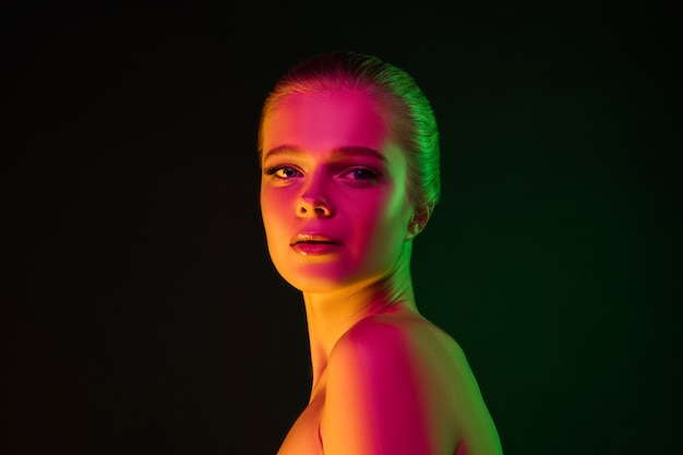 Portrait of female fashion model in neon light on dark studio background.