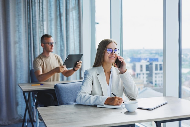 Portrait of a female manager in formal attire doing office work and talking on the phone a successful european female boss in optical glasses for vision correction posing at her desk