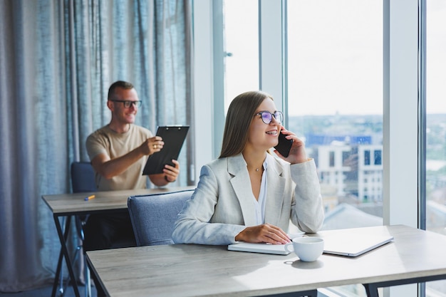 Portrait of a female manager in formal attire doing office work and talking on the phone a successful european female boss in optical glasses for vision correction posing at her desk