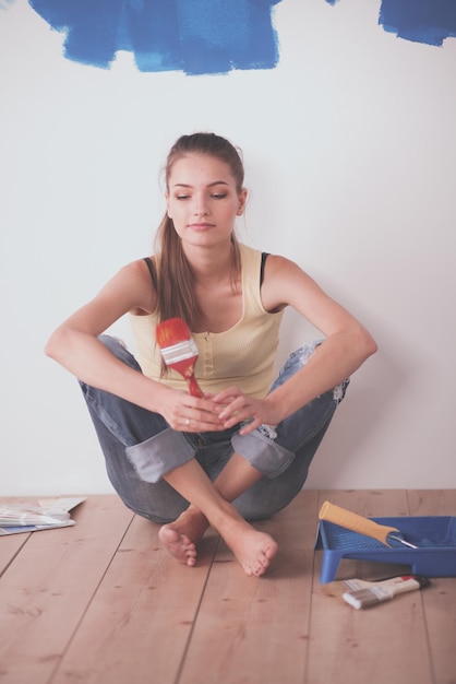 Portrait of female painter sitting on floor near wall after painting