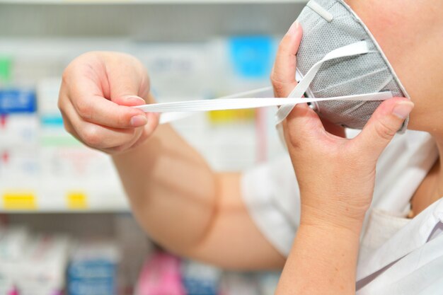 Portrait of female Pharmacist wear N95 mask on many medicine shelf background. Coronavirus (COVID-19)concept of disease, flu treatment and protection.