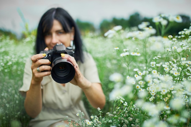 Portrait of Female photographer take photo outdoors on flower field landscape holding a camera