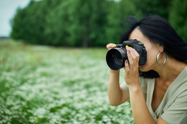 Portrait of Female photographer take photo outdoors on flower field landscape holding a camera