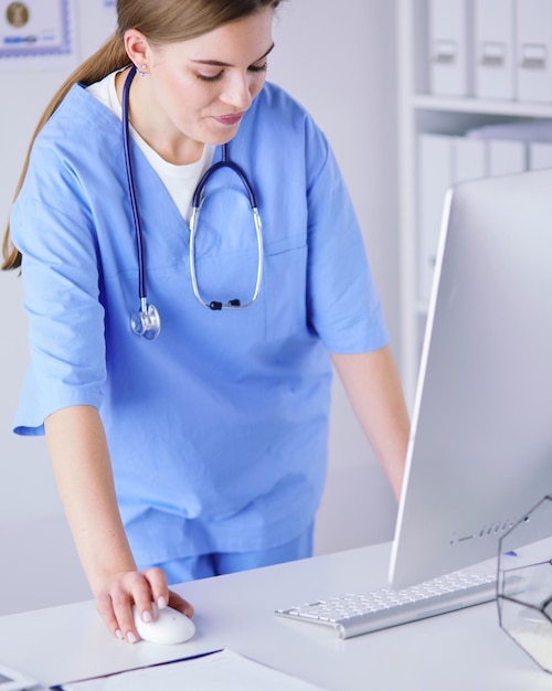 Portrait of female physician filling up medical form while standing near reception desk at clinic or