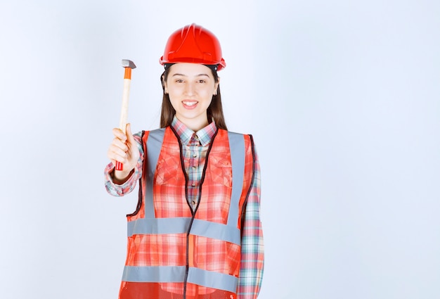 Portrait of female repairer in uniform holding hammer over white wall. 