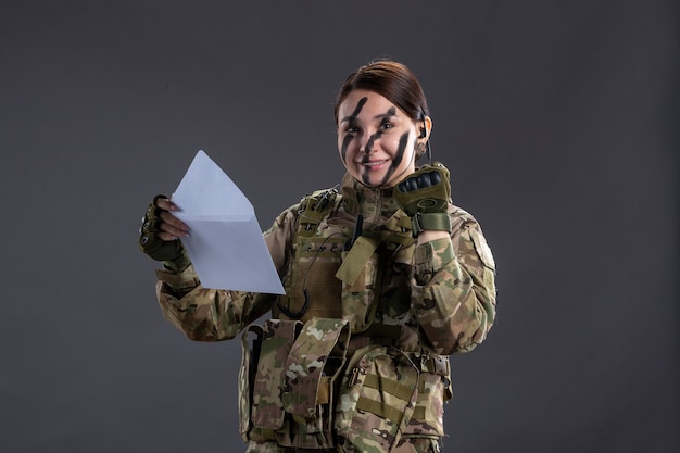 Portrait of female soldier reading letter on dark wall