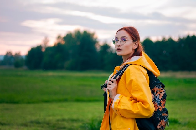 Portrait of a female tourist with a backpack in glasses wearing yellow coat Young woman travels during summer