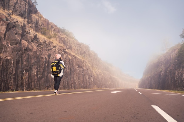 Portrait of a female traveler in casual clothes and backpack walking along the paved road.