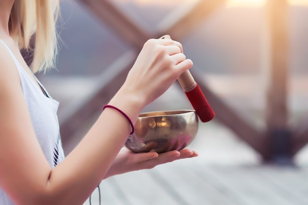 Photo portrait of female yoga teacher playing tibetan bowl or singing bell on a wooden bridge